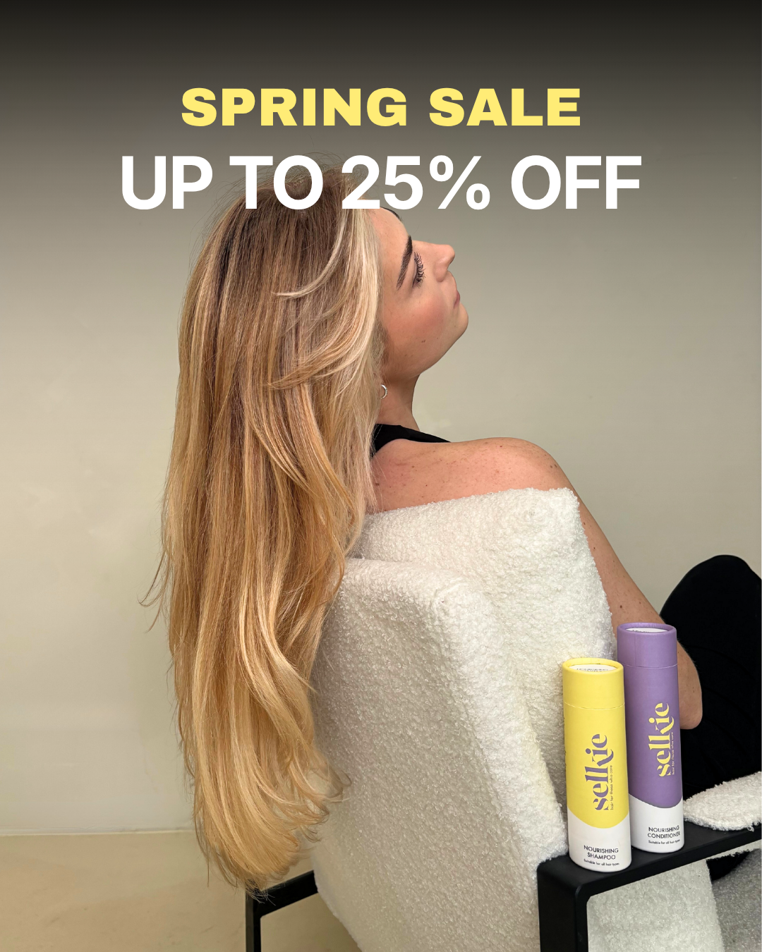 Woman with long blonde hair sitting in a chair with Selkie hair care products displayed.