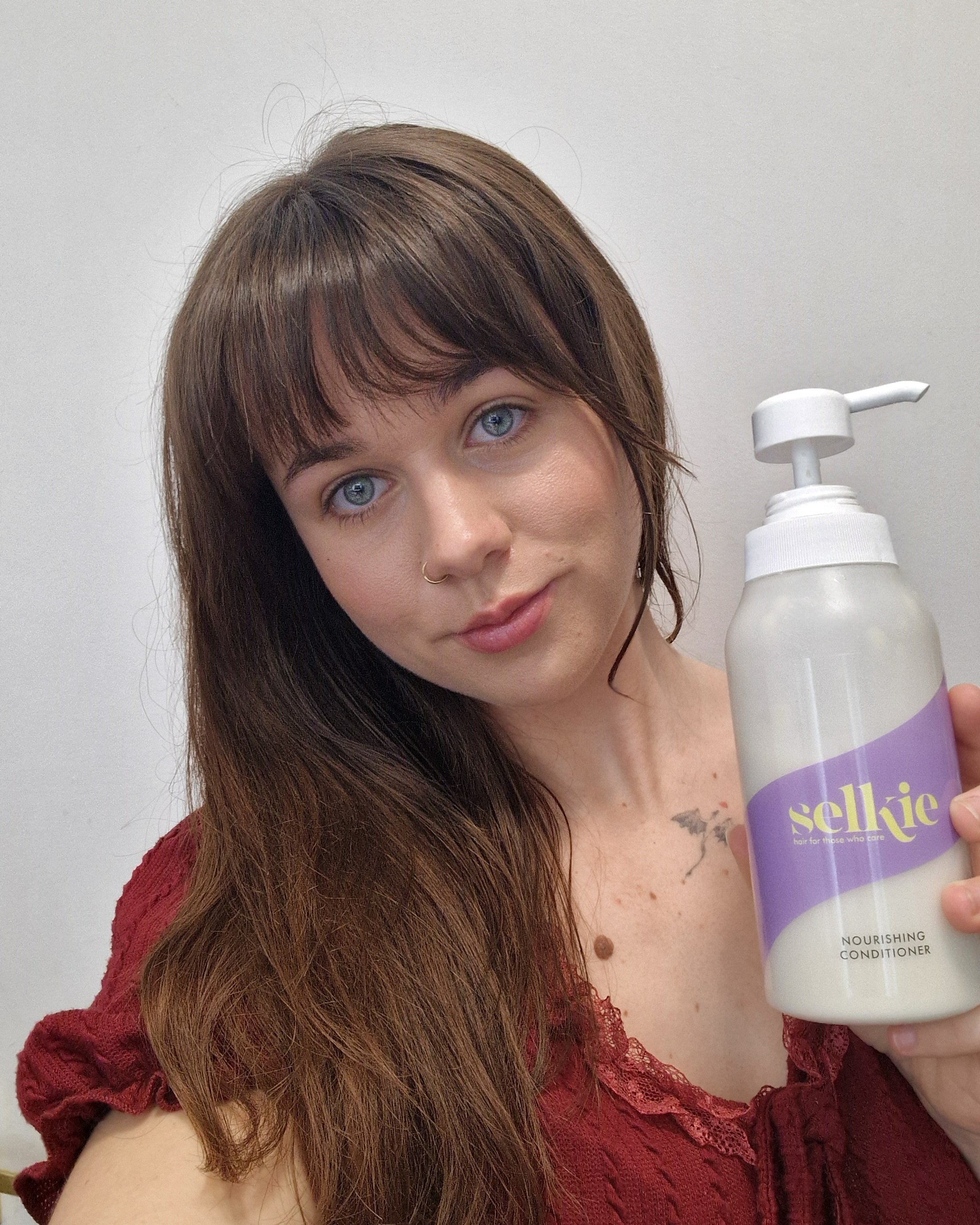 Woman holding a bottle of Selkie conditioner against a plain background